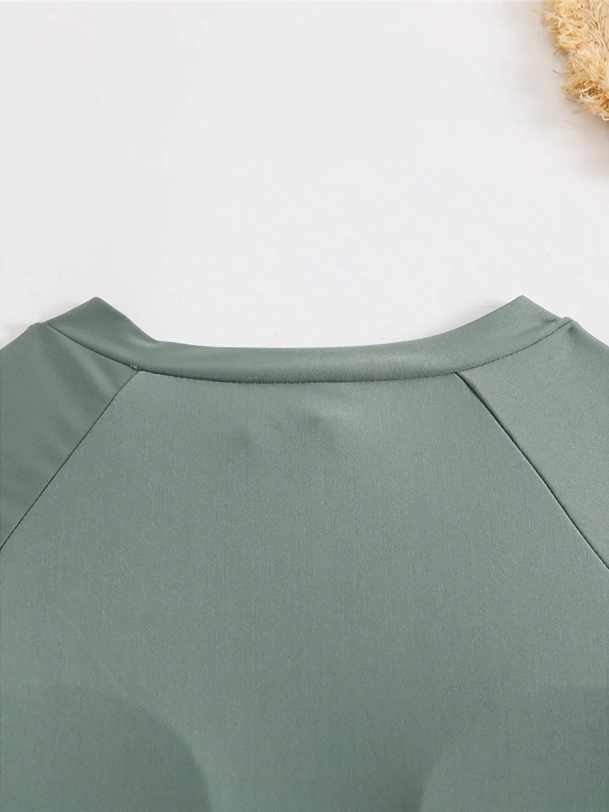 Gros plan sur l’encolure ronde du maillot vert foncé à manches longues, couture raglan visible
