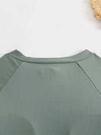 Gros plan sur l’encolure ronde du maillot vert foncé à manches longues, couture raglan visible