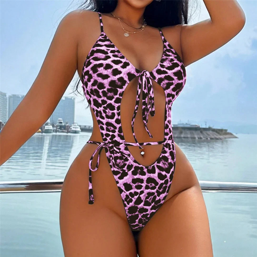 Maillot de bain une pièce échancré à nœud imprimé léopard rose porté de face, une main sur la hanche, sur fond de marina