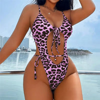 Maillot de bain une pièce échancré à nœud imprimé léopard rose porté de face, une main sur la hanche, sur fond de marina