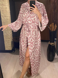 Robe de plage imprimée à manches longues col V rose portée de face par une femme, ceinture nouée et fente sur le devant