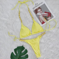 Bikini string tour de cou à anneau métallique froncé jaune posé à plat sur fourrure blanche, feuille de monstera