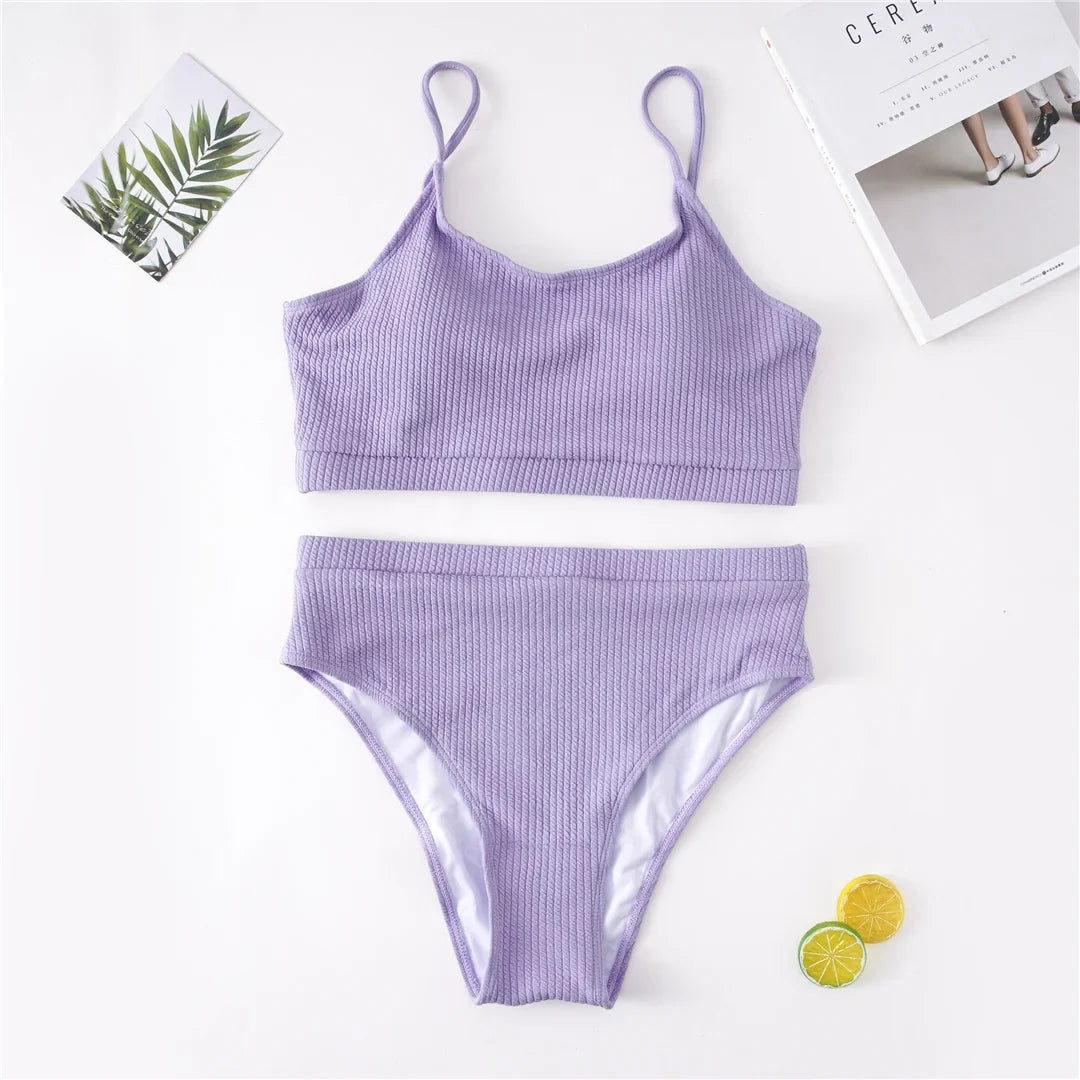 Bikini deux pièces grande taille côtelé taille haute violet à plat sur fond blanc, avec une feuille et un magazine