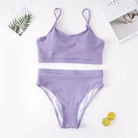 Bikini deux pièces grande taille côtelé taille haute violet à plat sur fond blanc, avec une feuille et un magazine