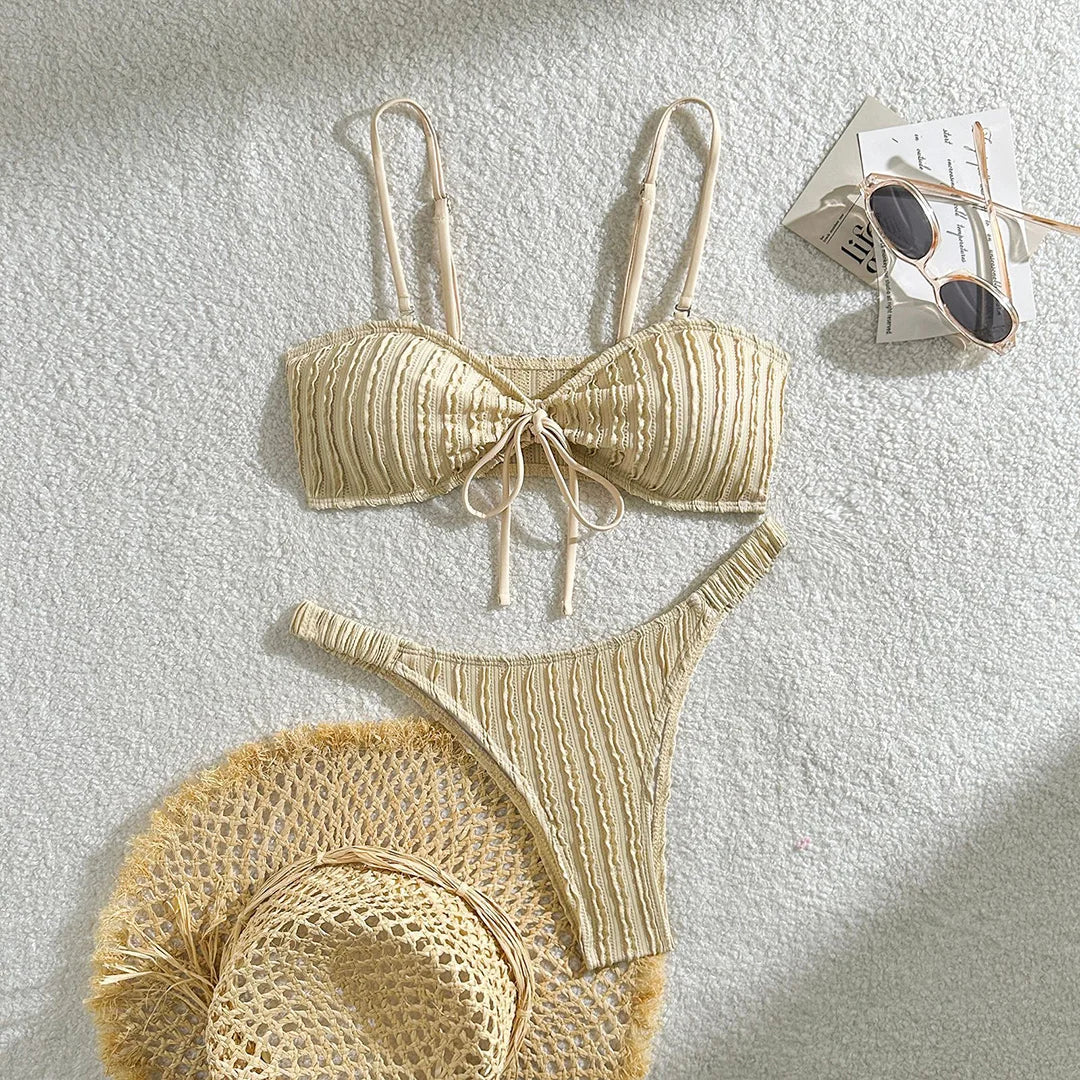 Bikini brésilien texturé froissé à nœuds beige posé à plat avec un chapeau en paille et des lunettes de soleil