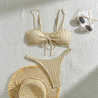 Bikini brésilien texturé froissé à nœuds beige posé à plat avec un chapeau en paille et des lunettes de soleil