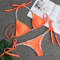 Bikini orné de strass brillants taille basse orange posé à plat sur un tapis gris, feuille verte et magazine