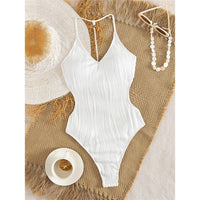Maillot de bain une pièce blanc texturé à plat sur un tapis en osier, bretelles fines et dos échancré, collier de perles à côté