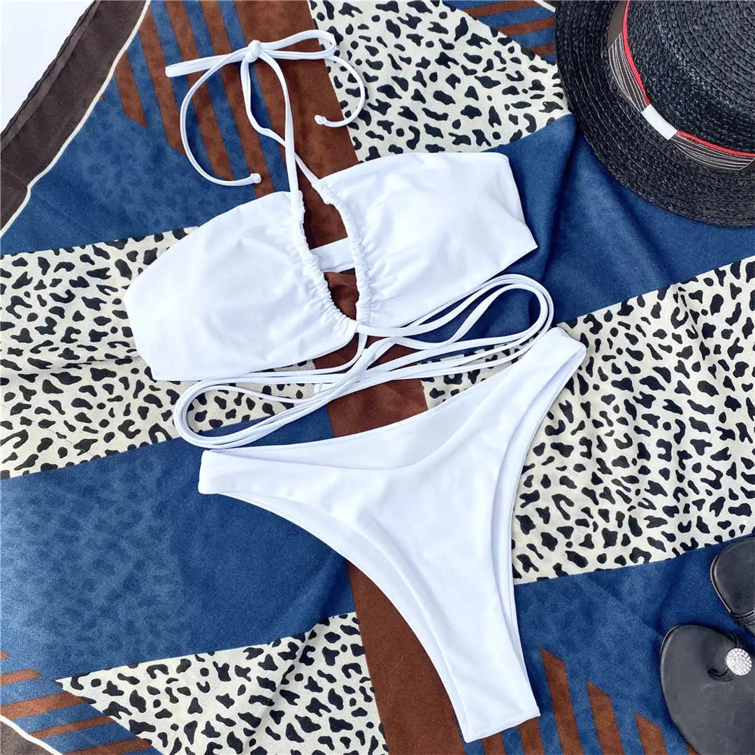Bikini tour de cou à lacets croisés sans armatures blanc posé à plat sur un foulard, avec chapeau noir et lunettes