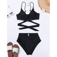 Bikini taille haute décolleté en V noir posé à plat sur fond blanc, haut à lanières croisées autour du buste et sandales en décor