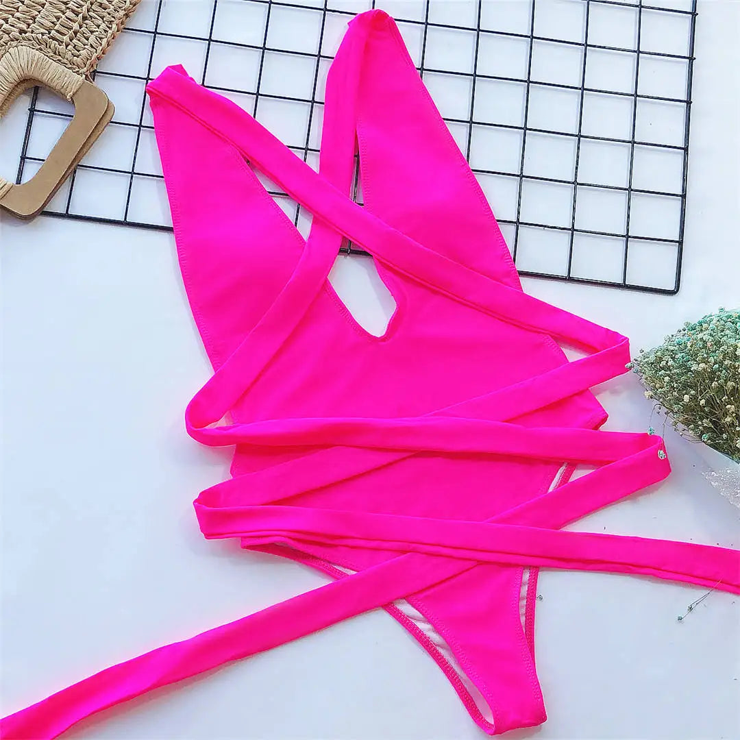 Maillot de bain une pièce triangle croisé rose fuchsia posé à plat sur une grille, lanières croisées déployées