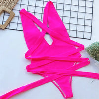 Maillot de bain une pièce triangle croisé rose fuchsia posé à plat sur une grille, lanières croisées déployées