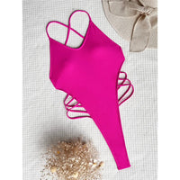 Maillot de bain une pièce rose fuchsia posé à plat sur un tissu blanc, avec lanières croisées sur les côtés