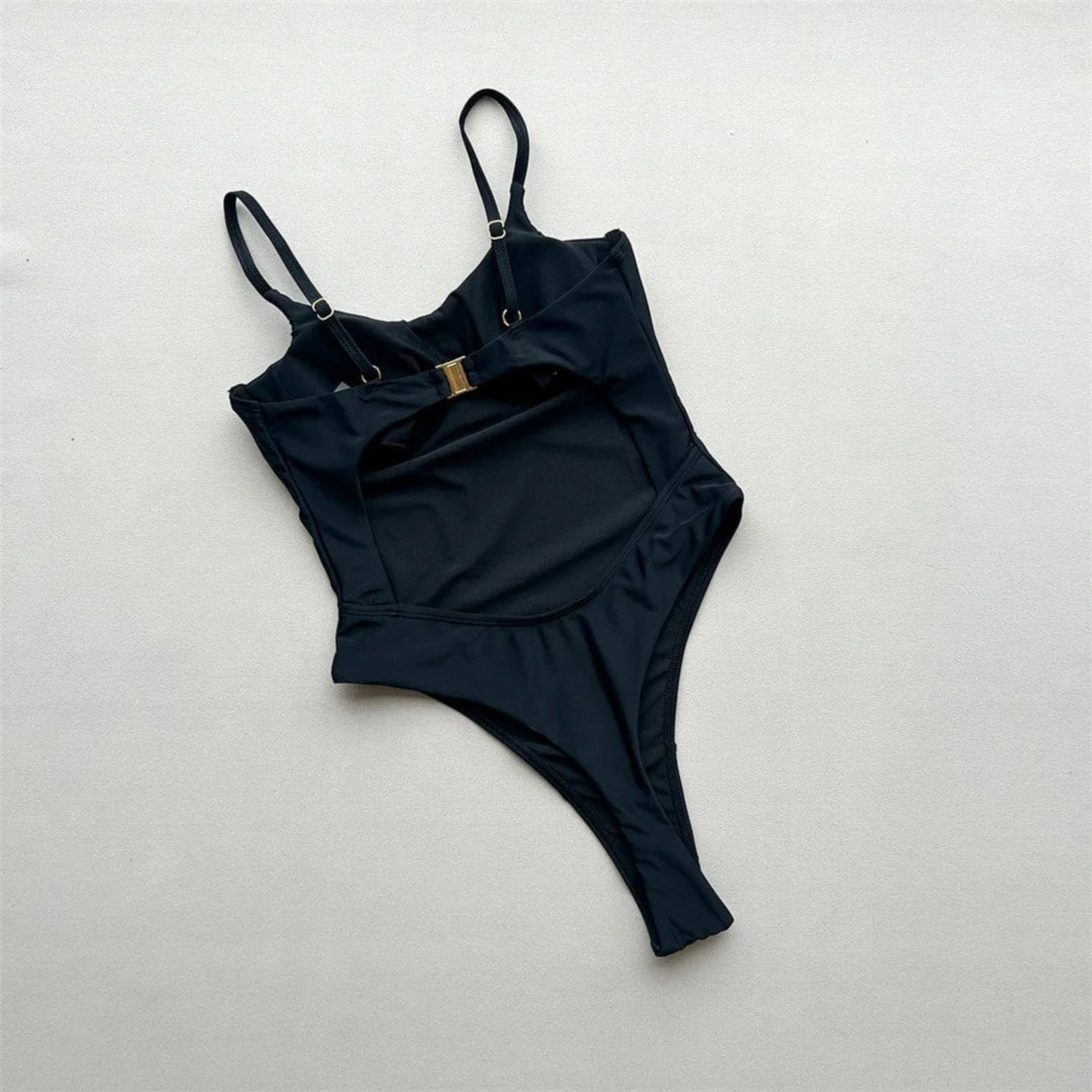 Maillot de bain une pièce échancré à découpes noir posé à plat de face sur fond clair, bretelles fines et boucle dorée