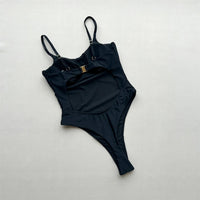 Maillot de bain une pièce échancré à découpes noir posé à plat de face sur fond clair, bretelles fines et boucle dorée