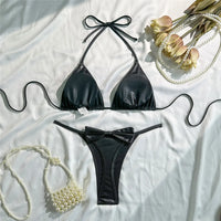 Bikini triangle brillant noir à nouer au cou posé à plat avec bas assorti, entouré de perles et de fleurs séchées