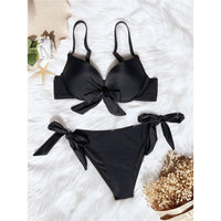 Bikini push-up noué avec armatures et rembourrage noir posé à plat sur fourrure blanche, longs nœuds sur le haut et le bas
