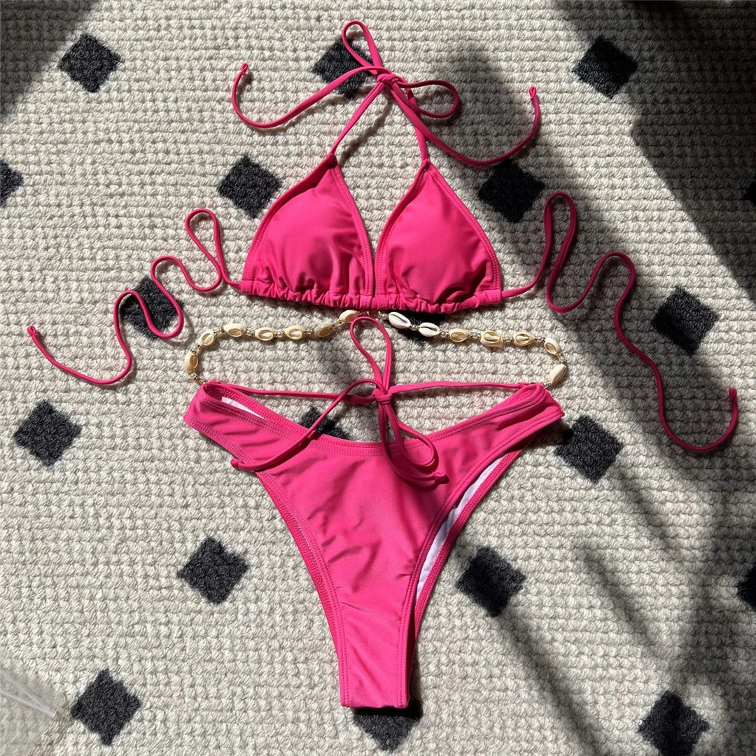 Bikini brésilien coquille rose fuchsia posé à plat sur un tapis à motifs, triangle sans armatures et chaîne de coquilles dorées