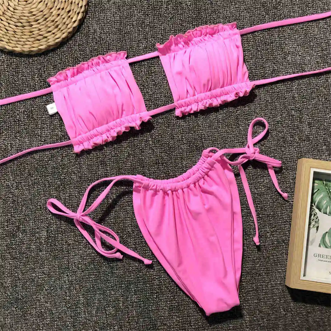 Bikini bandeau à volants bretelles réglables rose posé à plat sur un tapis gris, culotte à lacets