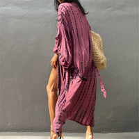 Tunique de plage imprimée manches longues à ceinture rose fuchsia portée de côté, sac en osier sur l'épaule