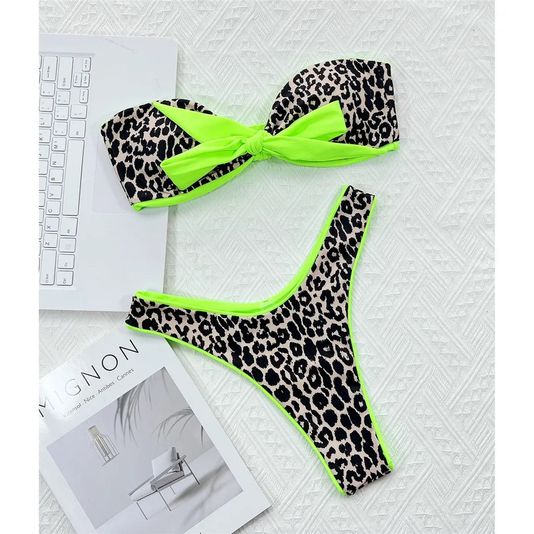 Bikini bandeau imprimé léopard posé à plat sur une table blanche, nœud vert fluo au centre et culotte assortie