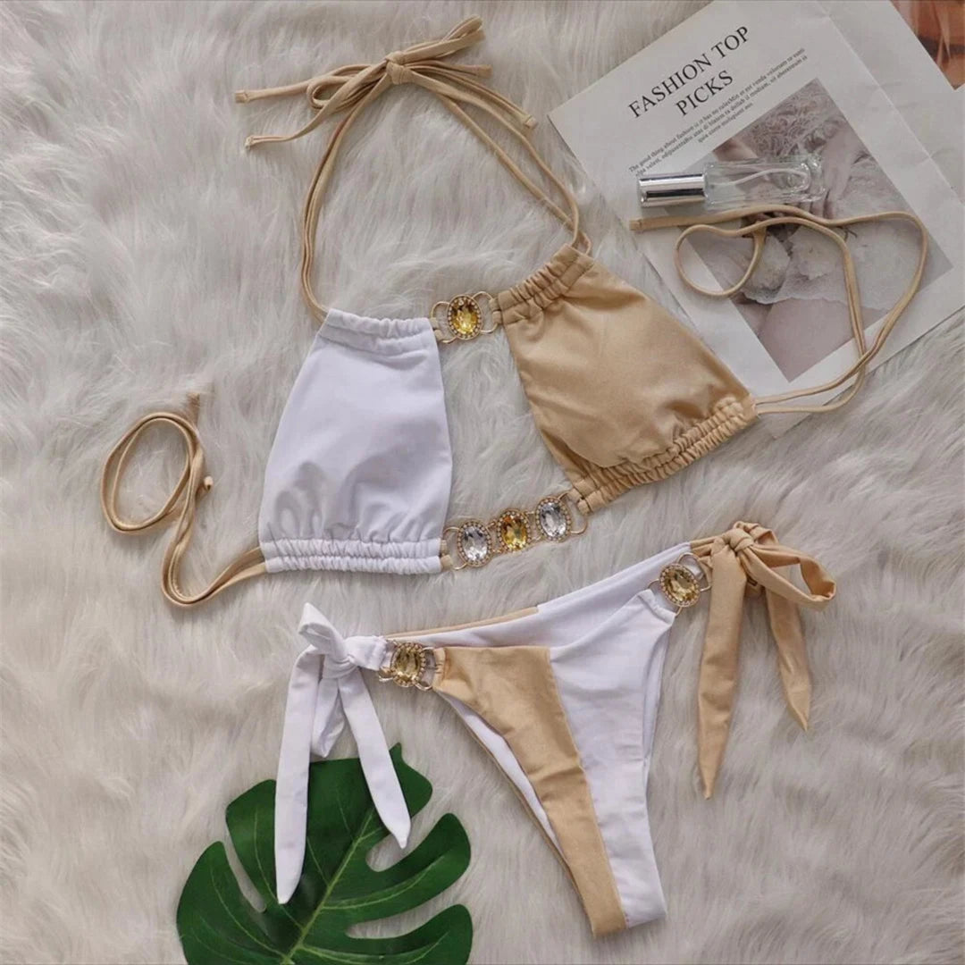Bikini strass blanc et beige posé à plat sur une fourrure blanche, haut beige et blanc avec anneaux dorés ornés de pierres jaunes