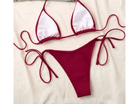 Bikini triangle bordeaux vu à plat côté intérieur doublé de blanc, lacets de nouage, posé sur un tissu blanc