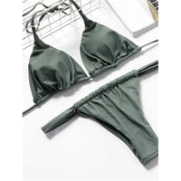 Bikini string triangle froncé vert militaire posé à plat sur une chaise en métal, bas taille basse à bandes larges