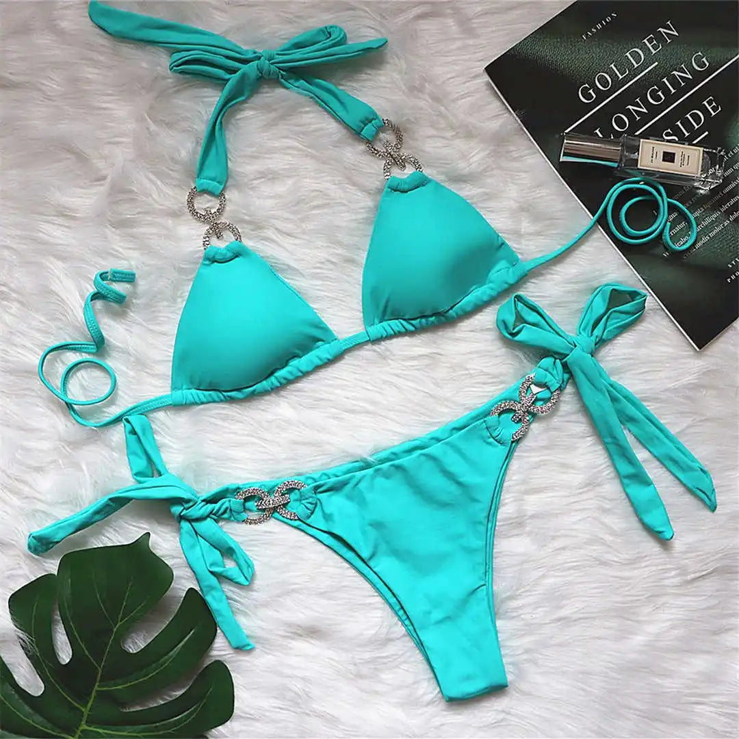 Bikini brésilien tour de cou à ornements strass vert turquoise posé à plat sur une fourrure blanche, près d'une feuille verte