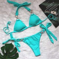 Bikini brésilien tour de cou à ornements strass vert turquoise posé à plat sur une fourrure blanche, près d'une feuille verte