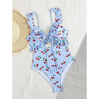 Maillot de bain une pièce à volants bleu clair à cerises posé à plat à côté d'un chapeau de paille, échancré