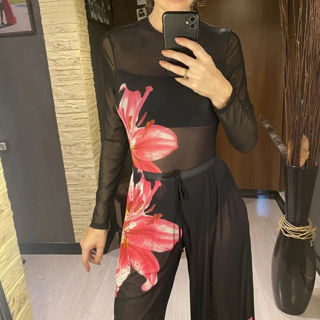 Ensemble noir en mesh porté de face, la fleur rose couvre la hanche et le pantalon, téléphone levé devant le visage