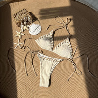 Bikini tour de cou beige à brides blanches posé à plat sur une natte ronde, coquillages et étoiles de mer