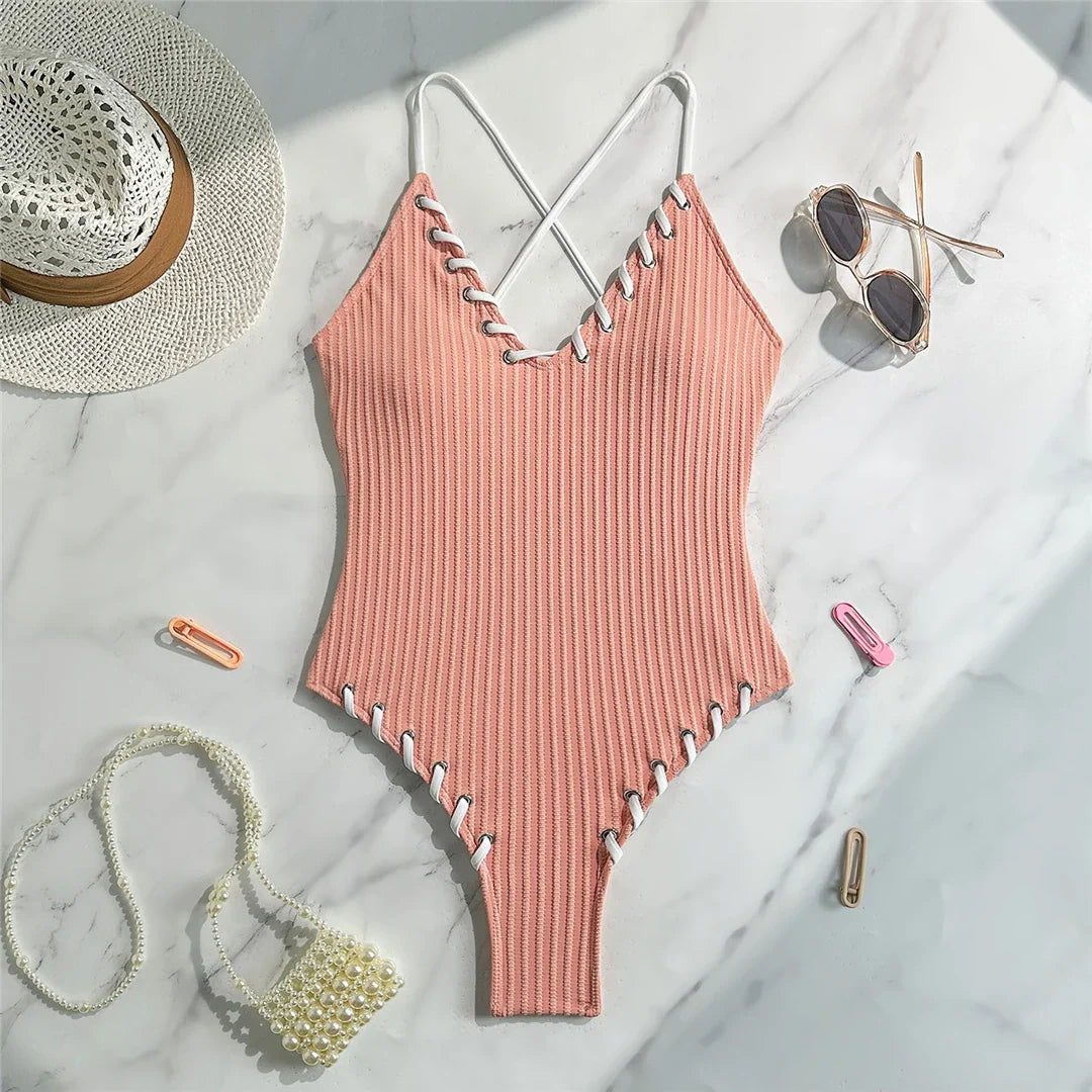 Maillot de bain une pièce côtelé rose posé à plat sur marbre, lacets blancs le long des bordures et bretelles croisées