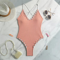 Maillot de bain une pièce côtelé rose posé à plat sur marbre, lacets blancs le long des bordures et bretelles croisées