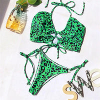 Bikini deux pièces tour de cou léopard vert à lacets posé à plat sur fond blanc, avec un flacon et des lettres décoratives