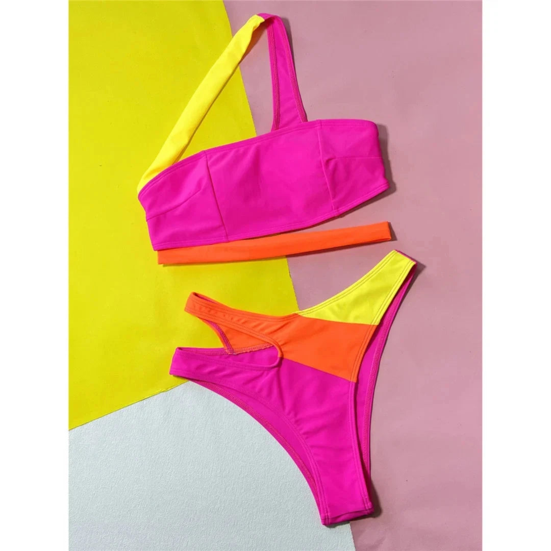 Bikini asymétrique rose vif, orange et jaune posé à plat sur fond color block, bretelle jaune et découpe orange