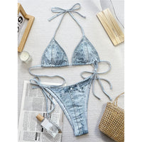 Bikini effet jean bleu clair posé à plat sur un journal, haut triangle à col halter et bas avec petits boutons