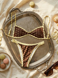 Bikini à pois marron et liseré jaune posé à plat sur un plateau argenté, entouré de macarons et de lunettes