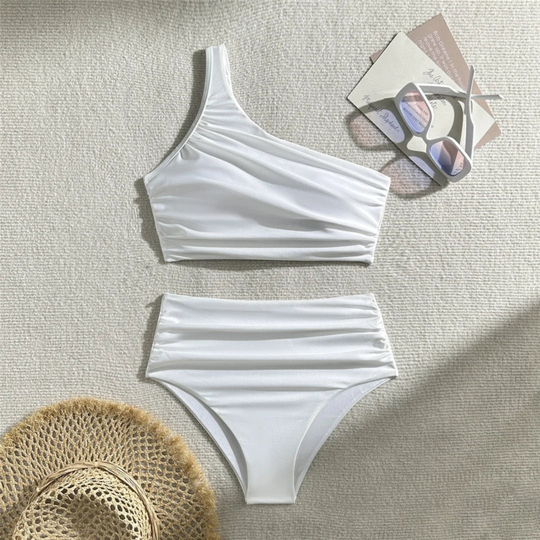 Bikini une épaule taille haute blanc froncé posé à plat sur fond clair, bretelle large et bas drapé