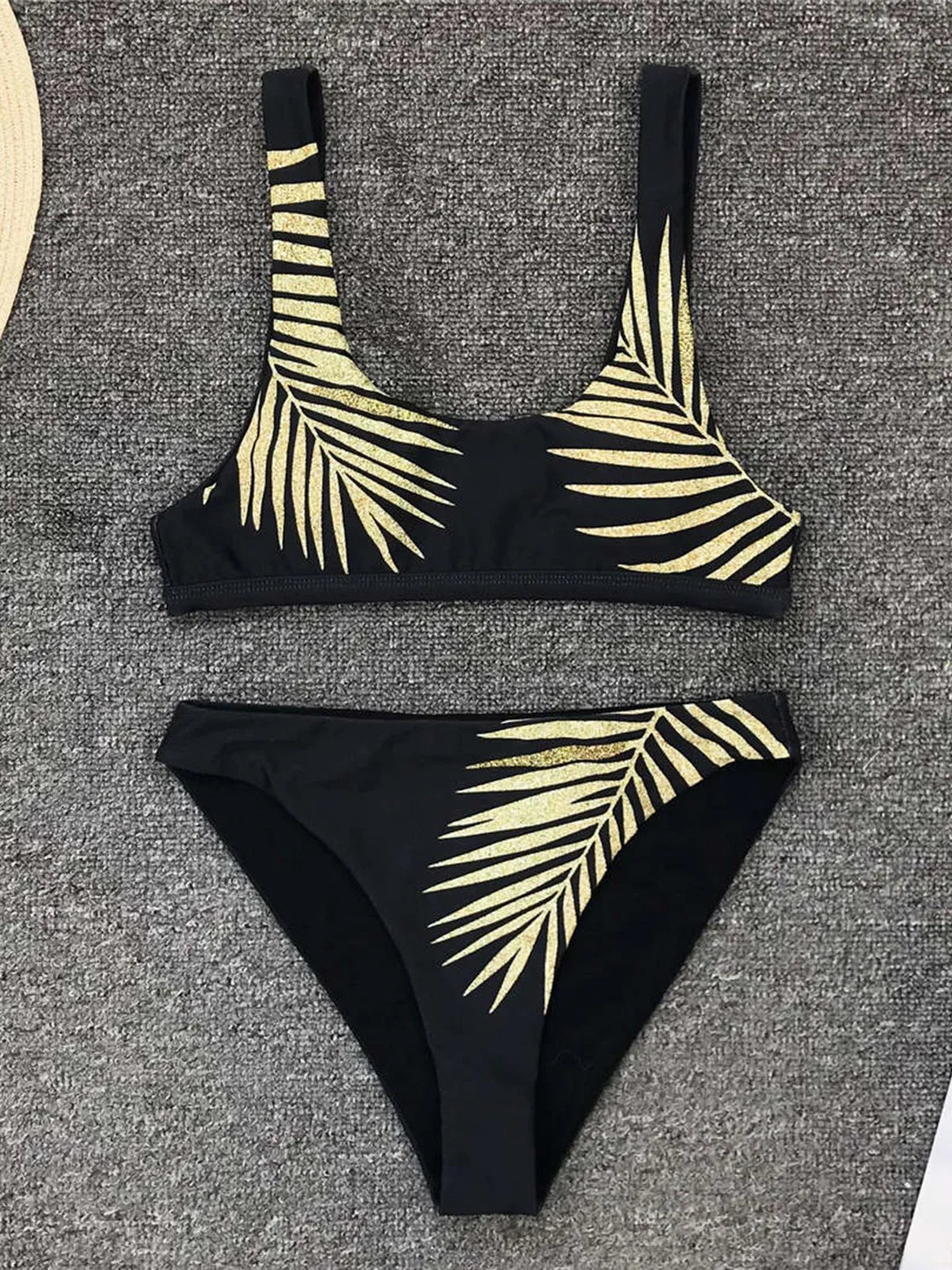 Bikini taille haute imprimé feuilles tropicales dorées sur fond noir posé à plat sur un tapis gris