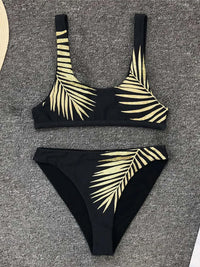 Bikini taille haute imprimé feuilles tropicales dorées sur fond noir posé à plat sur un tapis gris