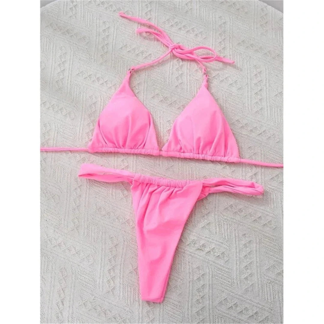 Bikini string triangle froncé rose posé à plat sur un tapis texturé, liens longs et bas froncé