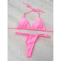 Bikini string triangle froncé rose posé à plat sur un tapis texturé, liens longs et bas froncé
