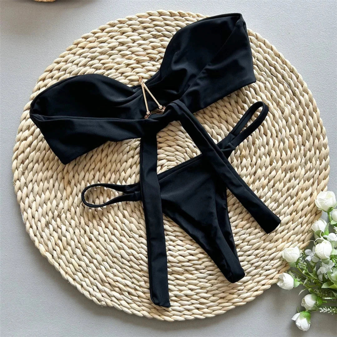 Bikini bandeau string échancré à étoile métallique noir déployé à plat, lanières croisées au centre et bordure lisse