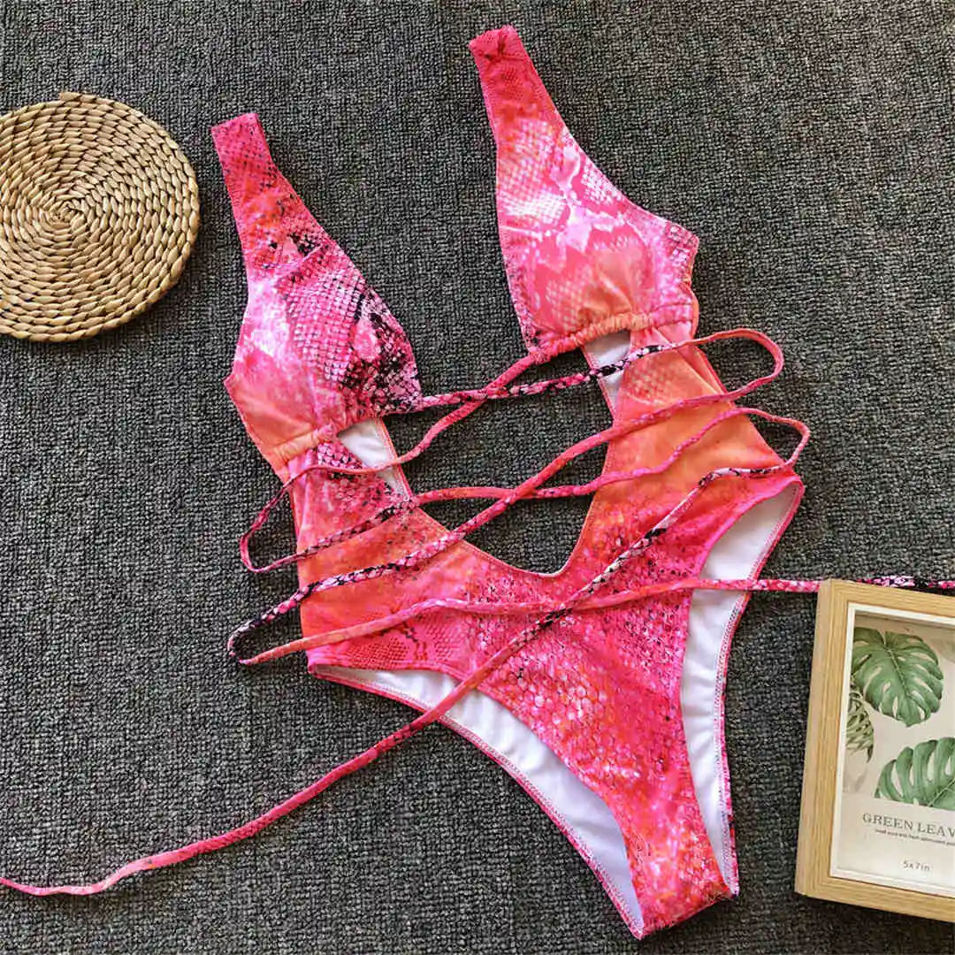 Monokini décolleté plongeant découpe ventre imprimé multicolore posé à plat sur du tissu gris, lacets longs et carte décorative