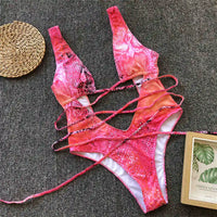 Monokini décolleté plongeant découpe ventre imprimé multicolore posé à plat sur du tissu gris, lacets longs et carte décorative