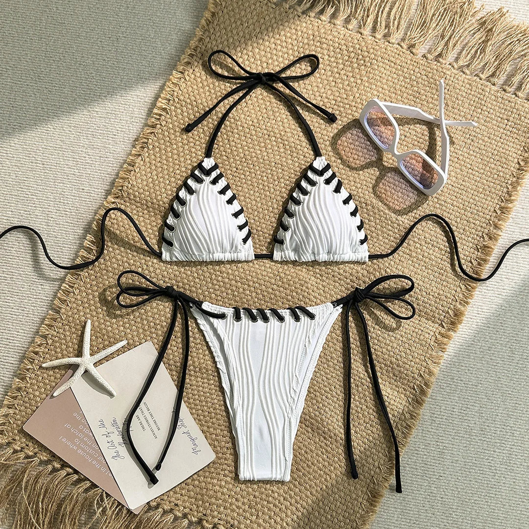 Bikini tour de cou blanc à brides noires posé à plat sur un tapis en jute, étoile de mer et carte postale
