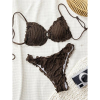 Bikini brésilien triangle effet froissé à volants marron posé à plat sur une couverture blanche, appareil photo à côté