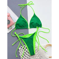 Bikini brésilien col halter taille basse vert foncé posé à plat avec téléphone rétro rose, liens verts fluo sur les côtés